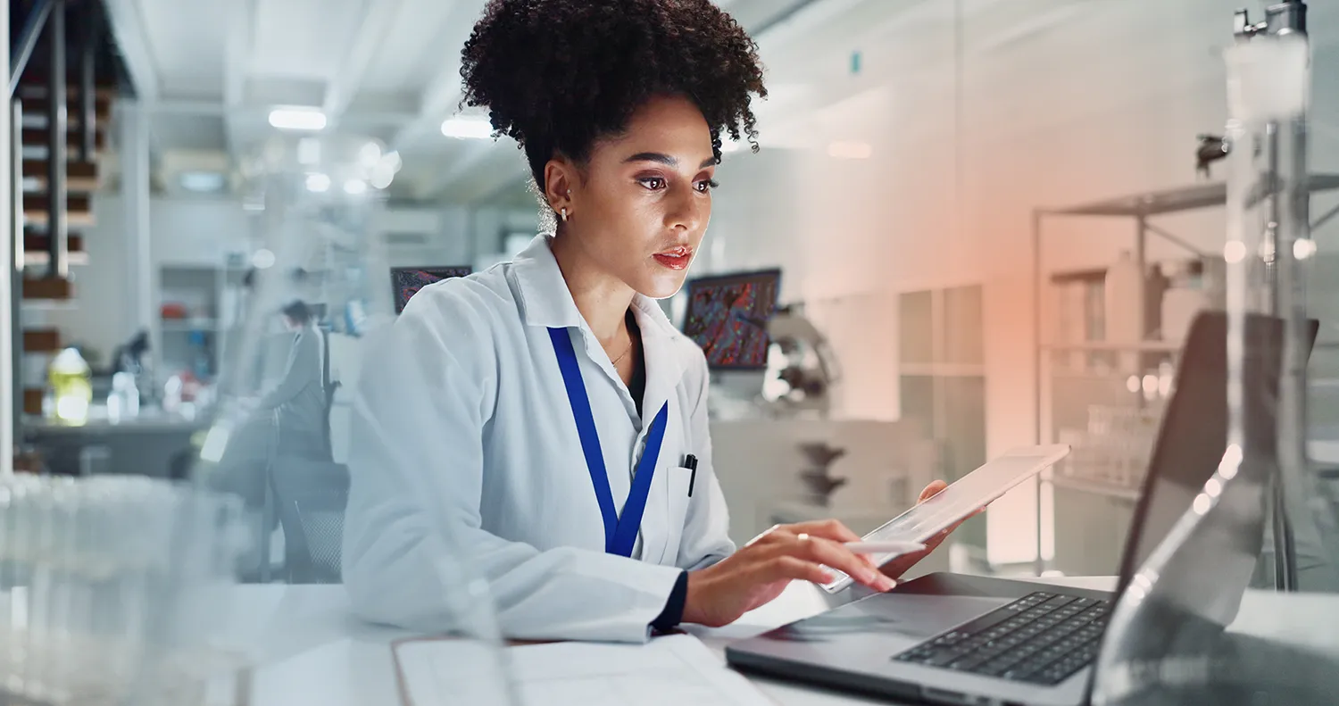 A scientist in a lab coat reviews results on a tablet in a bright laboratory.