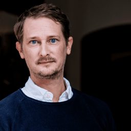 Portrait of Walter de Back in a dark sweater over a white collar.
