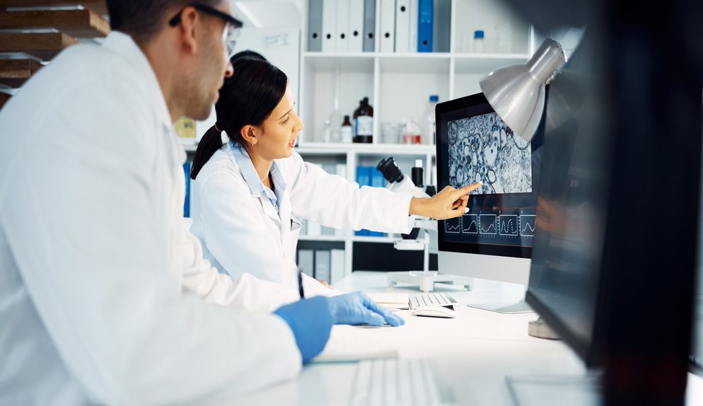 A scientist wearing glasses checks data on a tablet in the lab.