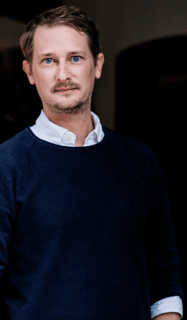 Portrait of Walter de Back in a dark sweater over a white collar.