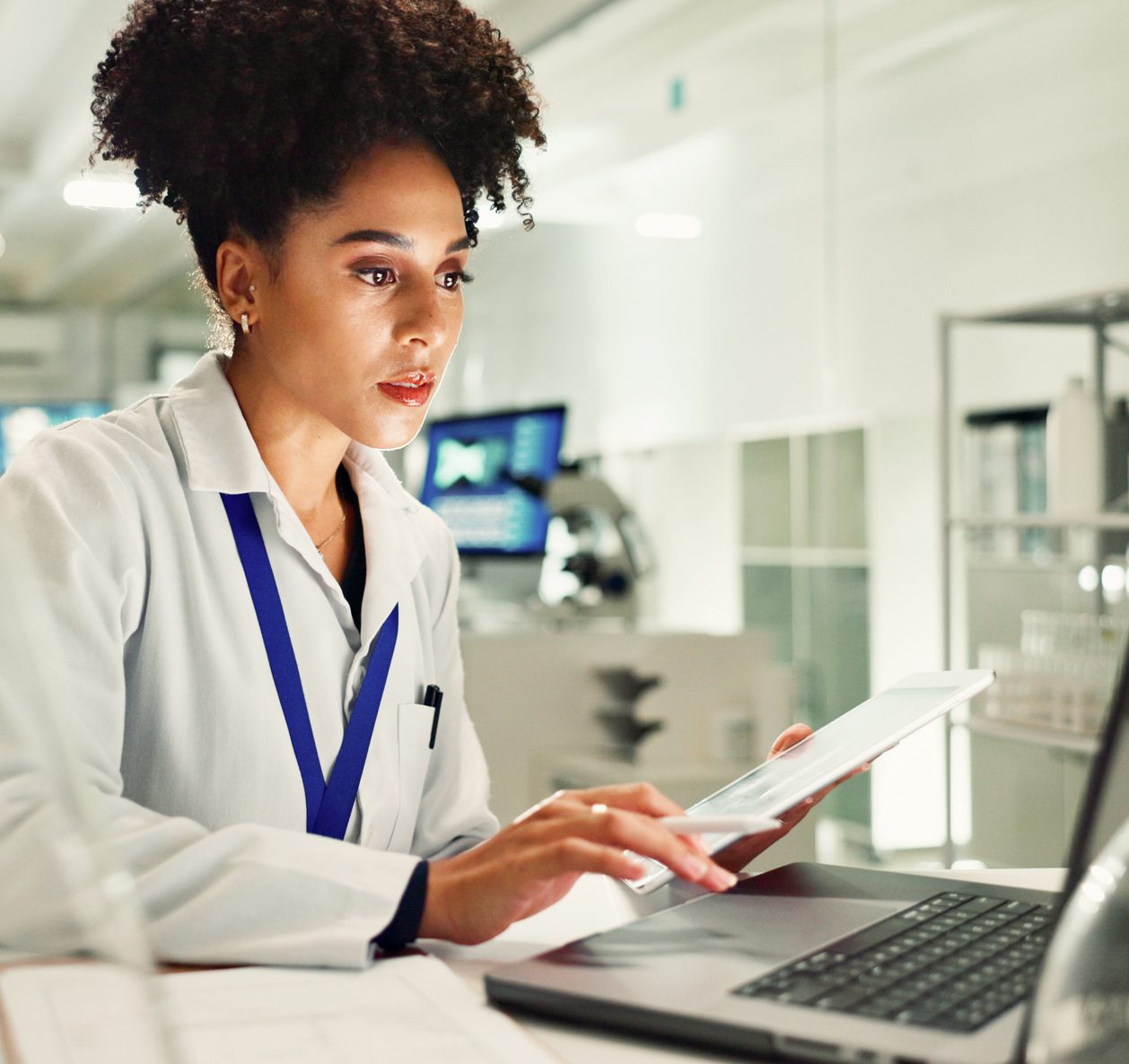A scientist in a lab coat reviews results on a tablet in a bright laboratory.