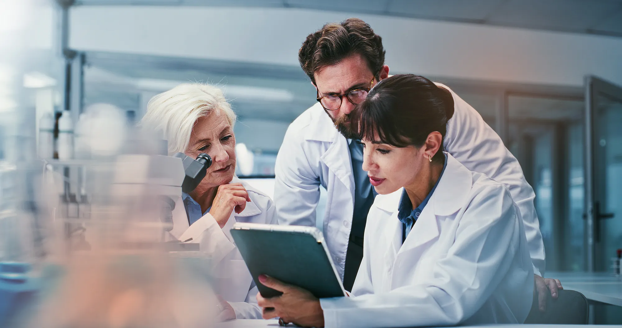 Three scientists gather around a tablet in a bright laboratory.
